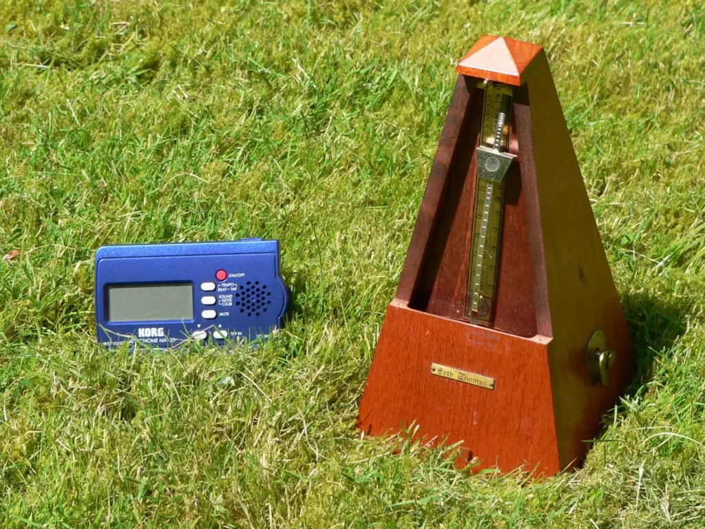 Electronic metronome next to a wooden mechanical metronome on grass